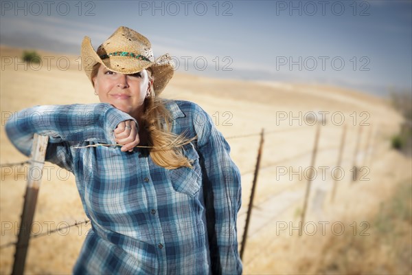 Beautiful cowgirl against barbed wire fence in field