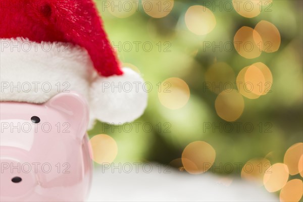 Pink piggy bank wearing red and white santa hat on snowflakes with abstract green and golden background