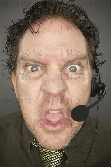 Irate businessman wearing a phone headset against a grey background