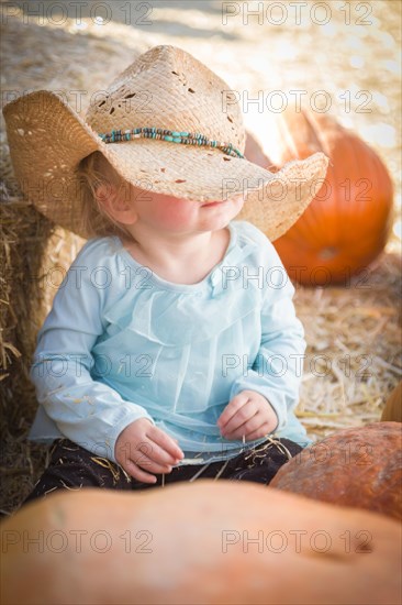 Adorable baby girl with cowboy hat in a country rustic setting at the pumpkin patch