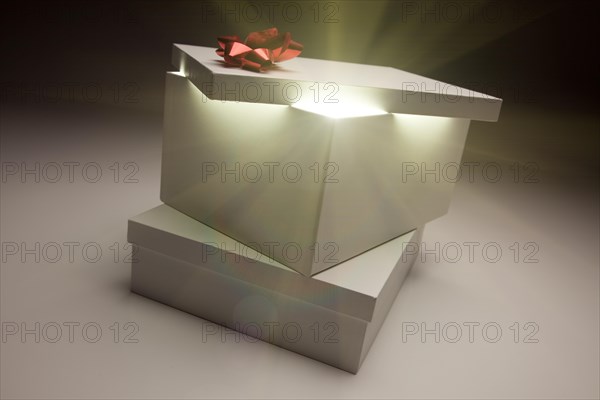 Gift box with red bow lid revealing very bright contents on a gradated background