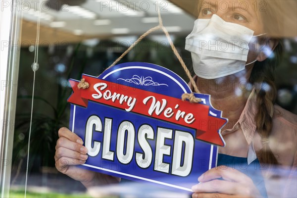 Female store owner wearing medical face mask turning sign to closed in window