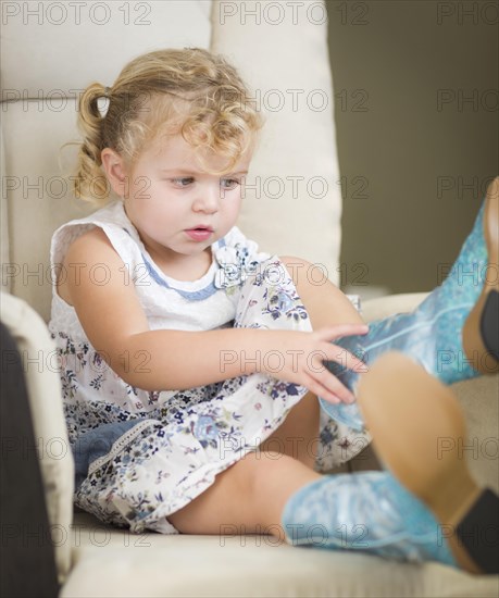 Adorable blonde haired blue eyed little girl putting on cowboy boots