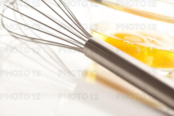Hand mixer with eggs in a glass bowl on a reflective white background