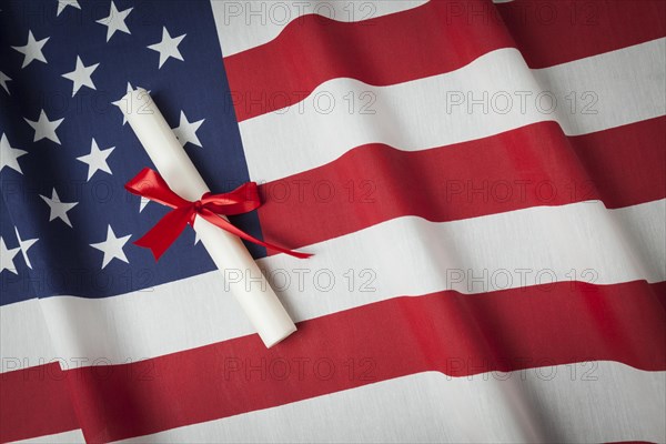 Red ribbon wrapped diploma resting on american flag with copy space