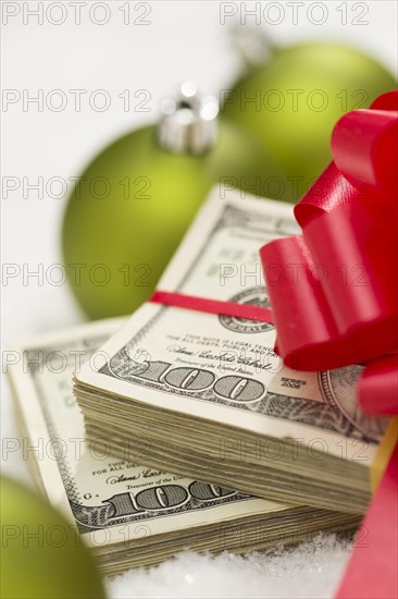 Stack of one hundred dollar bills with red bow near green christmas ornaments on snow flakes