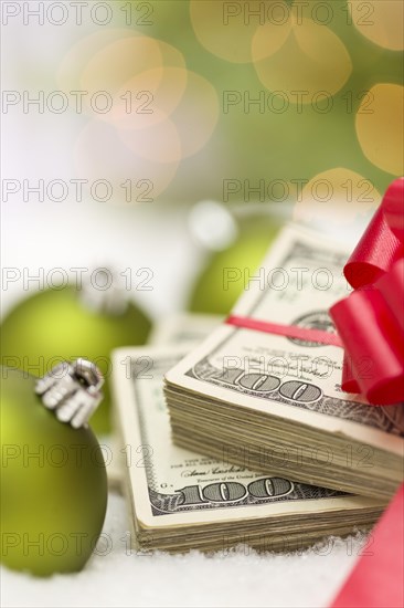 Stack of one hundred dollar bills with red bow near green christmas ornaments on snow flakes