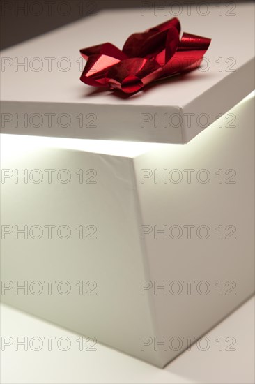 Gift box with red bow lid revealing very bright contents on a gradated background