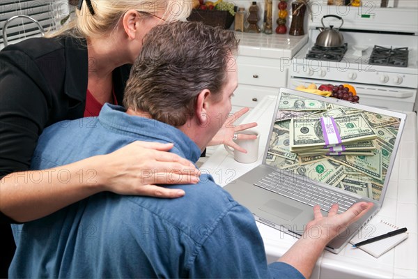 Couple in kitchen using laptop to earn or win money. screen can be easily used for your own message or picture. picture on screen is my copyright as well