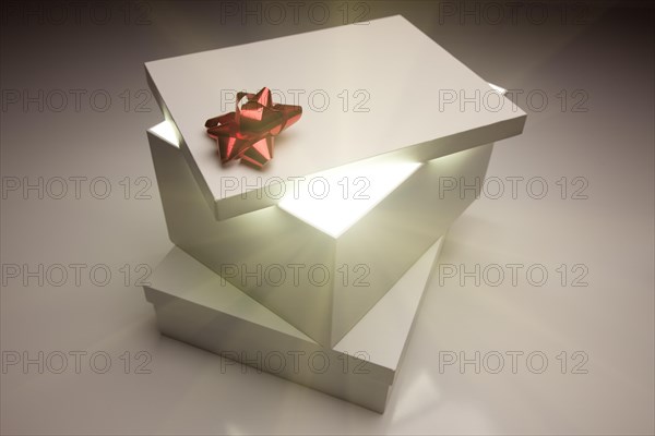 Gift box with red bow lid revealing very bright contents on a gradated background