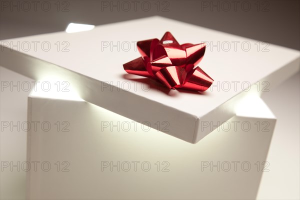 Gift box with red bow lid revealing very bright contents on a gradated background