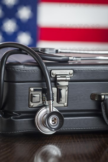 Leather briefcase and stethoscope resting on table with american flag behind