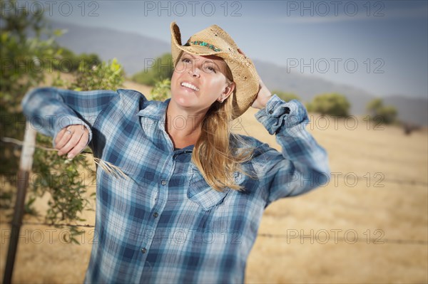 Beautiful cowgirl against barbed wire fence in field