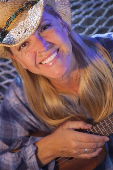 Beautiful evening portrait of cowgirl near campfire playing her ukulele