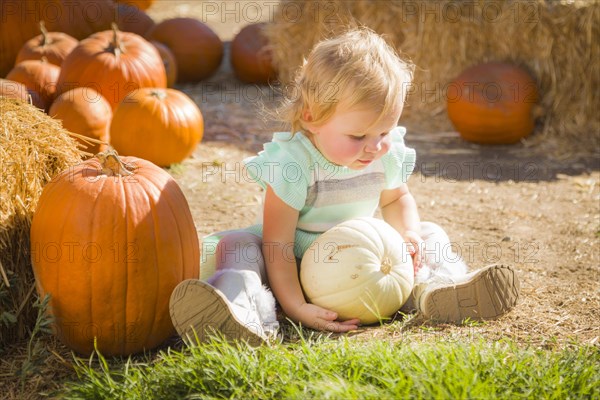 Adorable baby girl holding a pumpkin in a rustic ranch setting at the pumpkin patch