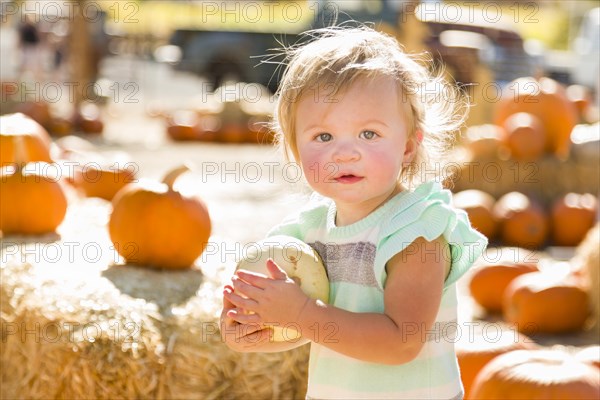 Adorable baby girl holding a pumpkin in a rustic ranch setting at the pumpkin patch