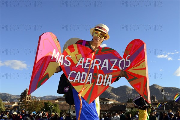 Stilt walkers with sign More hugs every day at parade on eve of Inti Raymi