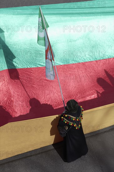 Kurdish woman demonstrates in front of the unfurled flag of the autonomous region of Kurdistan