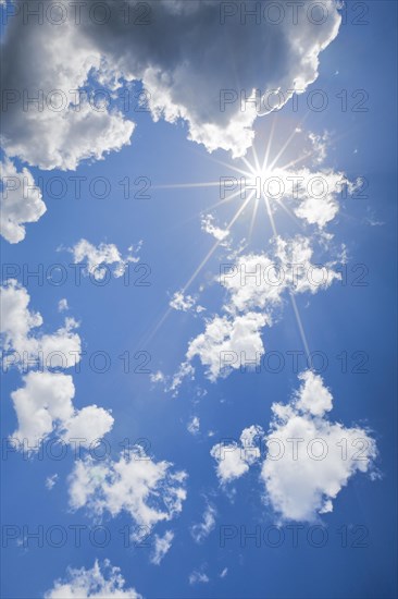 Sun star in the blue sky between isolated source clouds in the backlight