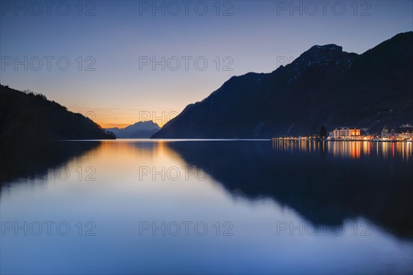 Illuminated lakeside promenade of Brunnen and view over Lake Lucerne at sunset with Mount Pilatus in the background