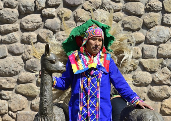 Indigenous man in colorful traditional costume in front of an Inca wall