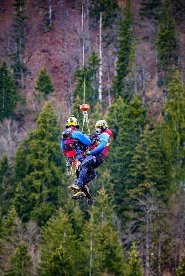 Two flight rescuers of the Bergwacht Bayern hang in the air on a wire rope