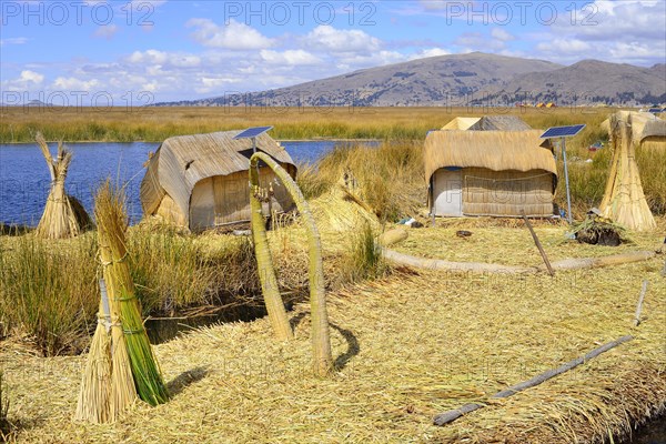 Reed bundles in front of reed huts with solar cells on a floating island of the Uro