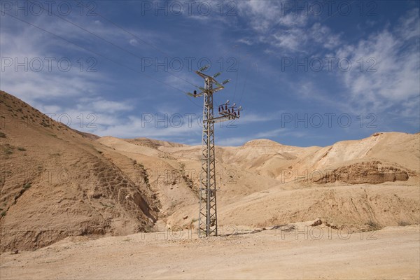 High-voltage pylon in front of mountain range with blue sky in Negev desert