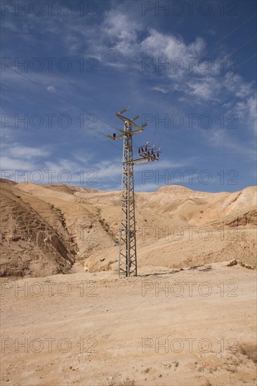 High-voltage pylon in front of mountain range with blue sky in Negev desert