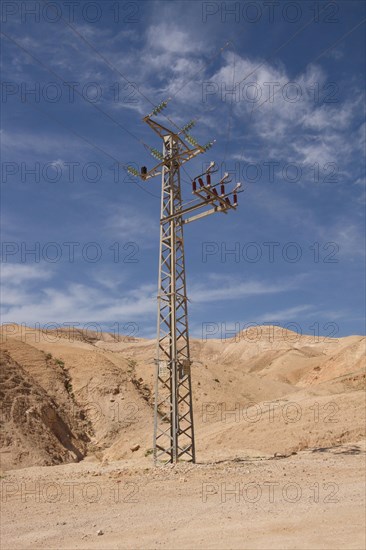 High-voltage pylon in front of mountain range with blue sky in Negev desert