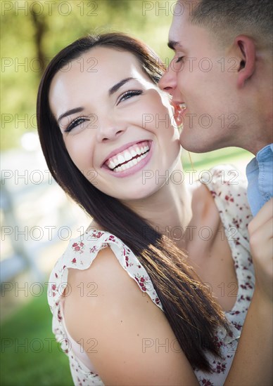 Happy mixed-race romantic couple whispering in the park