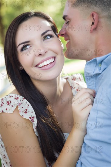 Happy mixed-race romantic couple whispering in the park