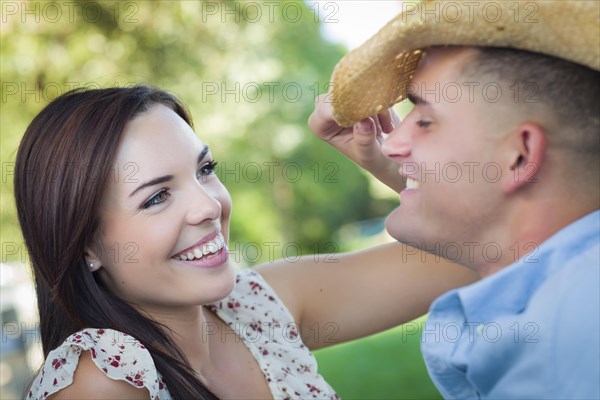 Happy mixed-race romantic couple with cowboy hat flirting in the park