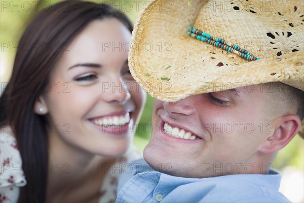 Happy mixed-race romantic couple with cowboy hat flirting in the park