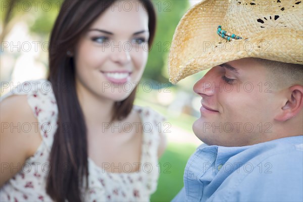 Happy mixed-race romantic couple with cowboy hat flirting in the park