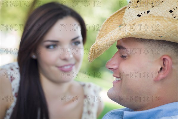 Happy mixed-race romantic couple with cowboy hat flirting in the park