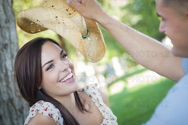 Happy mixed-race romantic couple with cowboy hat flirting in the park