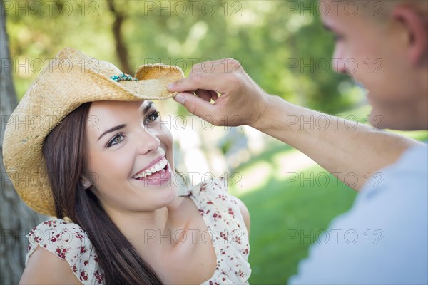 Happy mixed-race romantic couple with cowboy hat flirting in the park