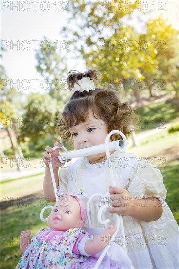 Adorable young baby girl playing with her baby doll and carriage outdoors