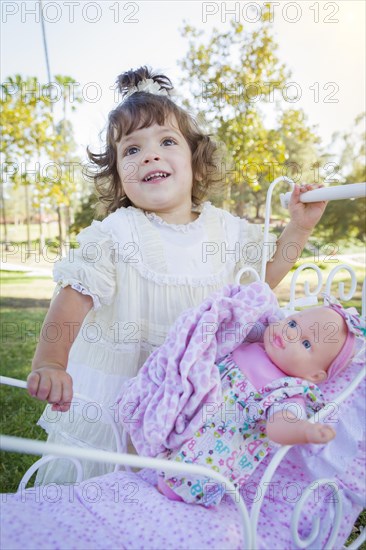 Adorable young baby girl playing with her baby doll and carriage outdoors