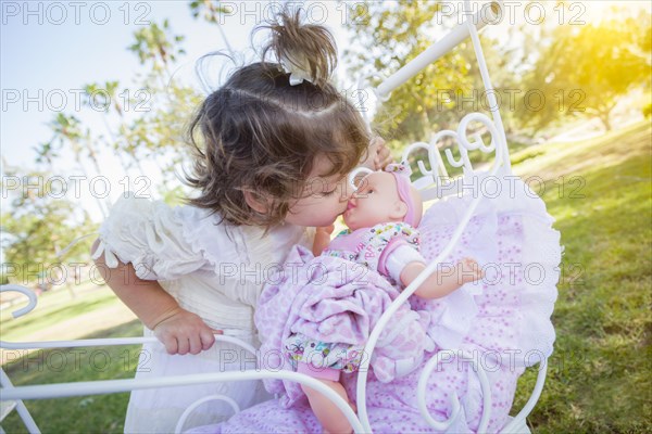 Adorable young baby girl playing with her baby doll and carriage outdoors