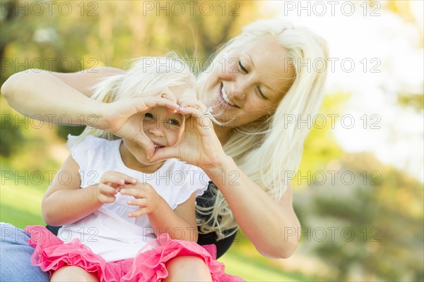 Cute little girl with mother making heart shape with hands outdoors