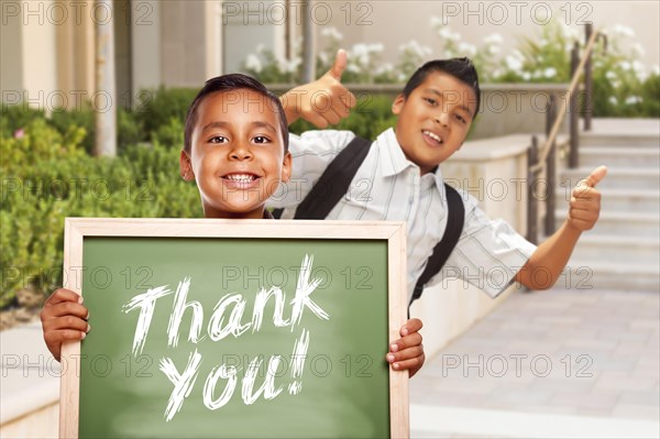 Happy hispanic boys giving thumbs up holding thank you chalk board outside on school campus