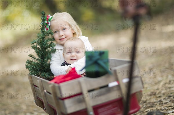 Baby brother and sister being pulled in wagon with christmas tree and gifts outdoors