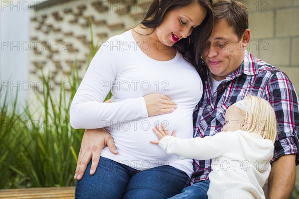 Adorable baby girl puts her hand on stomach of mommy as daddy looks on