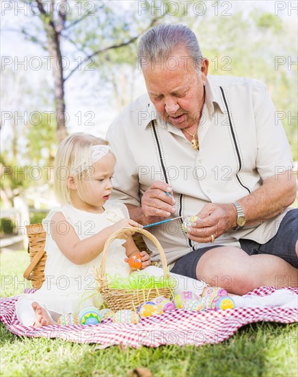 Loving grandfather and granddaughter coloring easter eggs together on picnic blanket at the park