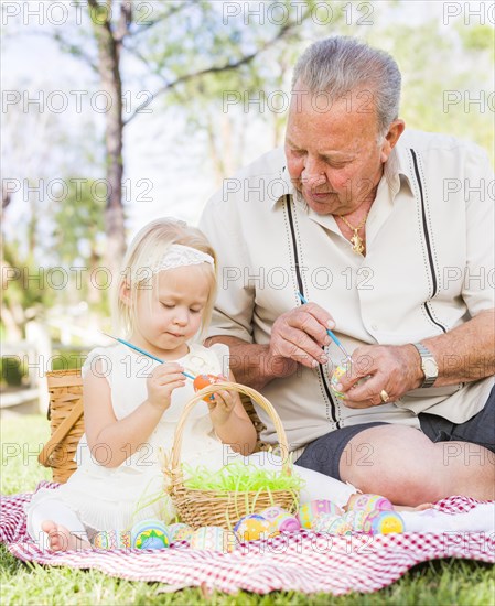 Loving grandfather and granddaughter coloring easter eggs together on picnic blanket at the park