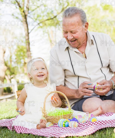 Loving grandfather and granddaughter coloring easter eggs together on picnic blanket at the park