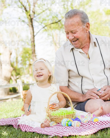 Loving grandfather and granddaughter coloring easter eggs together on picnic blanket at the park