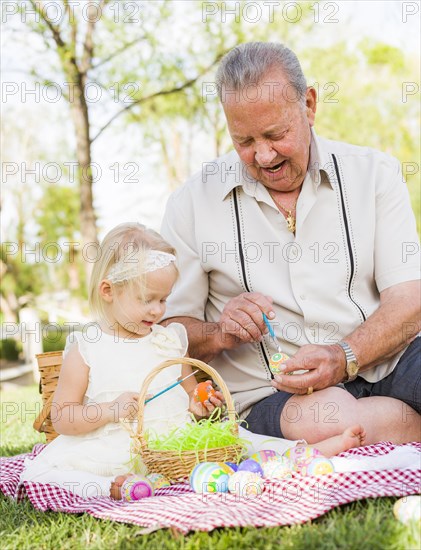 Loving grandfather and granddaughter coloring easter eggs together on picnic blanket at the park